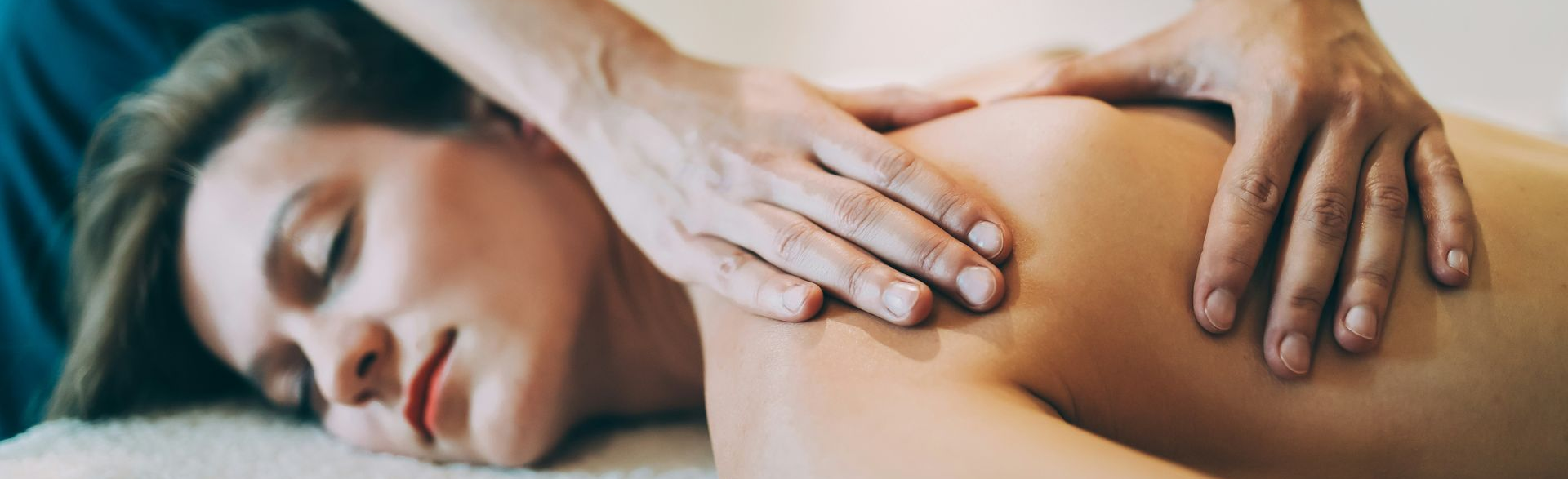 Woman receiving myofascial release in Las Vegas by a therapist using elbows. Soft lighting and plants in the background.