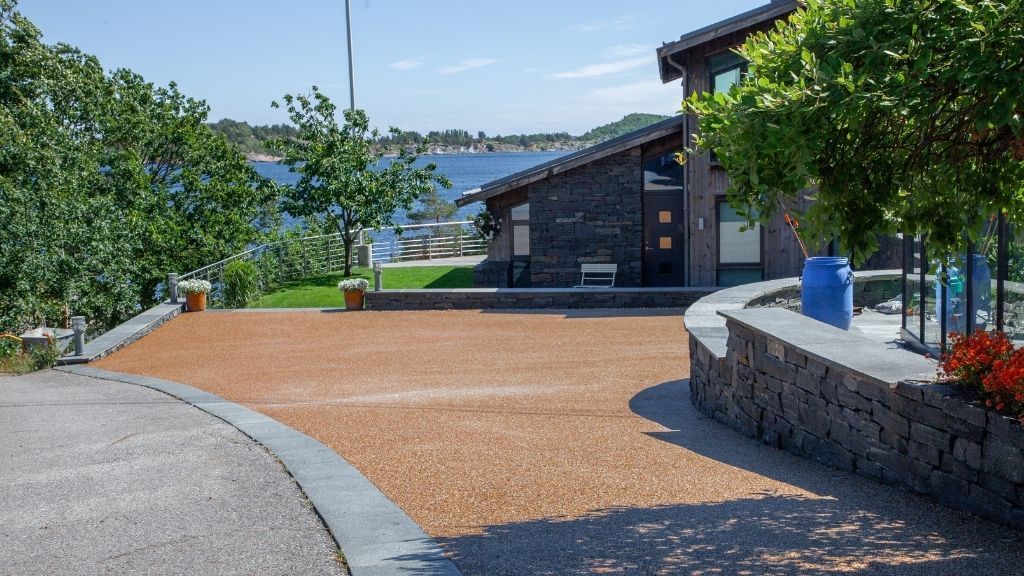 Resinbundet gårdsplass med natursteinsmur og utsikt mot sjøen.
