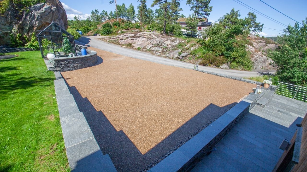 Resinbundet steindekke i uteområde med kantstein og plen.