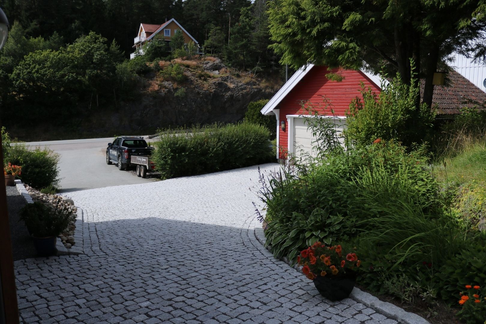 Brosteinslagt innkjørsel med hage og beplantning.
