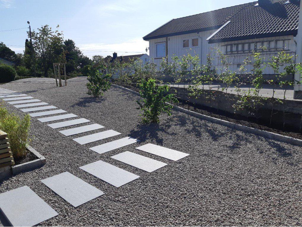 Gangsti med tråkkheller gjennom gruslagt hage.