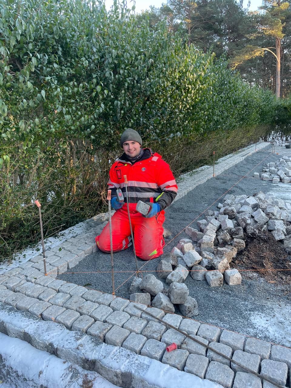 Arbeider foran hekk og steinlagt uteområde.