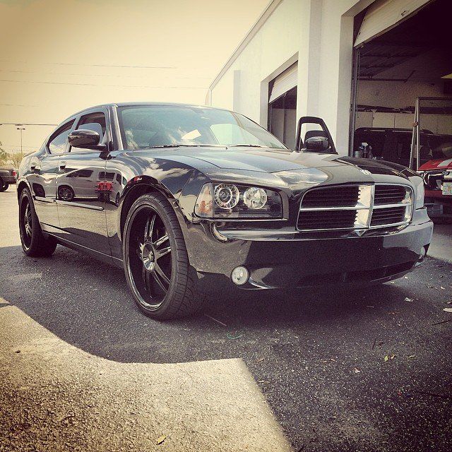 Black Dodge Charger parked outside a garage with an open door, sunny day.