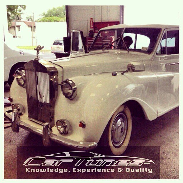 White vintage Rolls-Royce car with silver accents, parked in a garage, logo for 