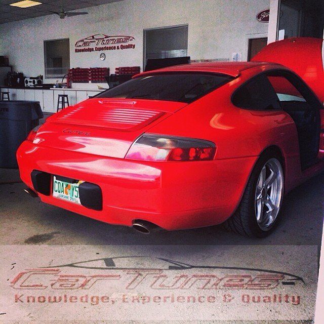 Red Porsche in a garage with the hood and door open, near a logo reading 