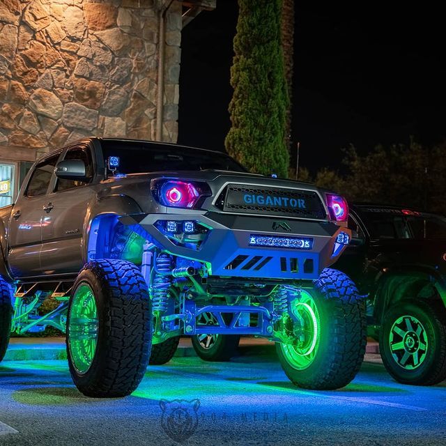Modified gray truck with neon blue and green underglow, parked at night.