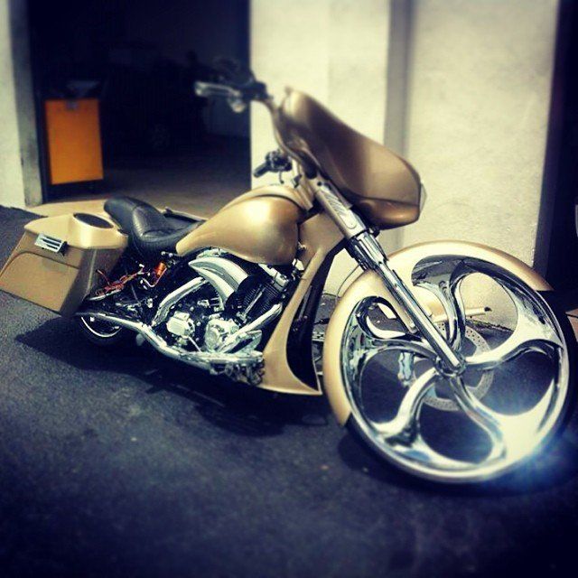 Gold custom motorcycle with large chrome wheels parked indoors.