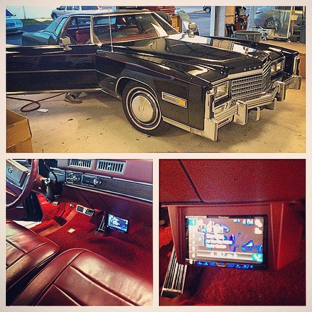 Black Cadillac Eldorado, red interior with touch screen, in a garage.