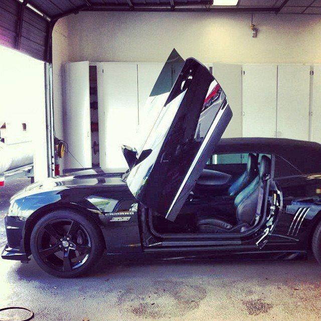 Black Camaro convertible with doors open upward, parked in a garage.