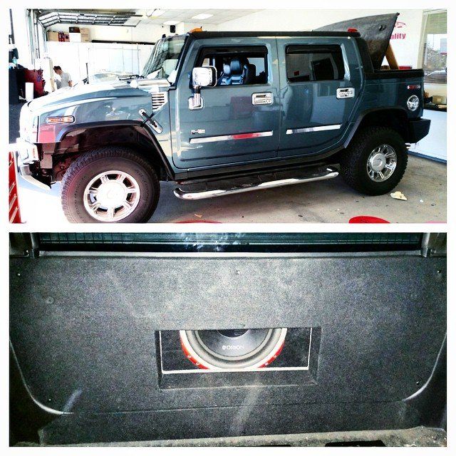Hummer H2 SUV in repair shop, with closeup of subwoofer in rear panel. Blue-green vehicle.