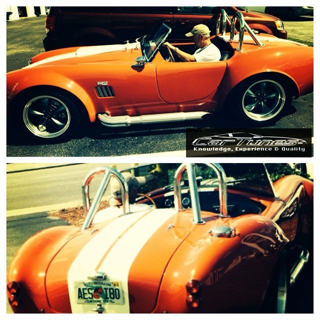 Orange Cobra car with white stripes, driver, parked outdoors.
