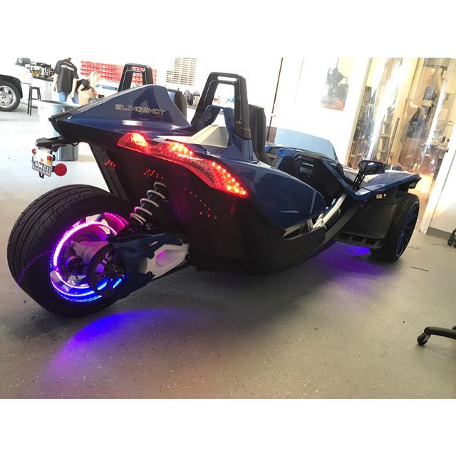 Blue Polaris Slingshot with custom LED lighting, parked indoors.