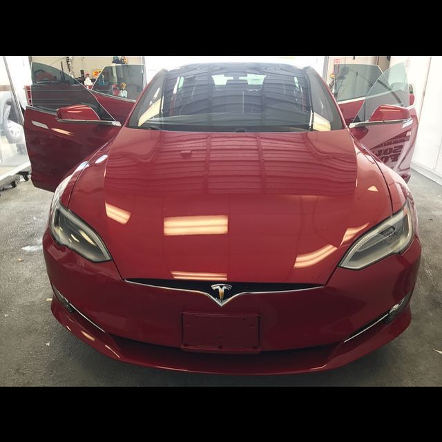 Red Tesla car with doors open, reflecting overhead lights.