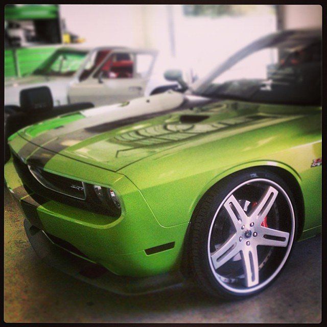 Green Dodge Challenger with black stripes and custom wheels, in a garage.