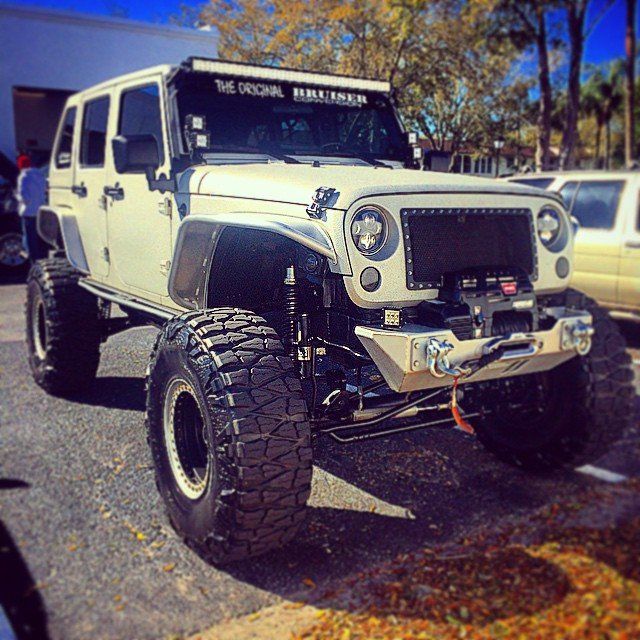 White lifted Jeep Wrangler with large tires, custom front bumper, and LED light bar.
