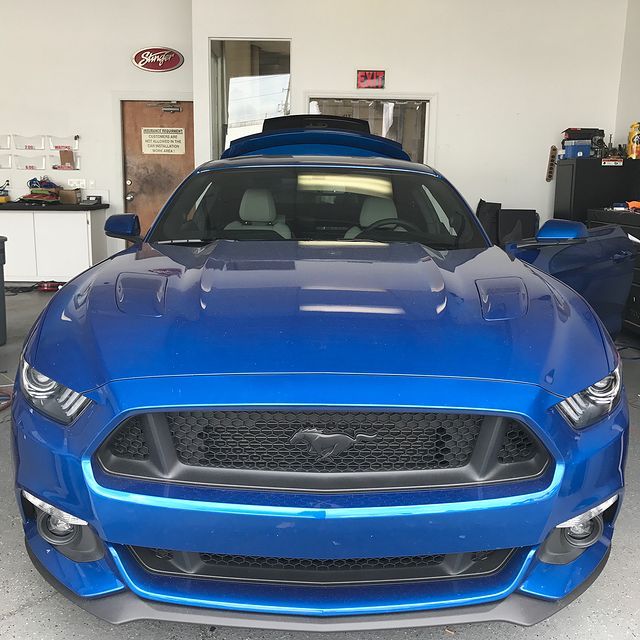 Blue Ford Mustang with black grill, in a garage.