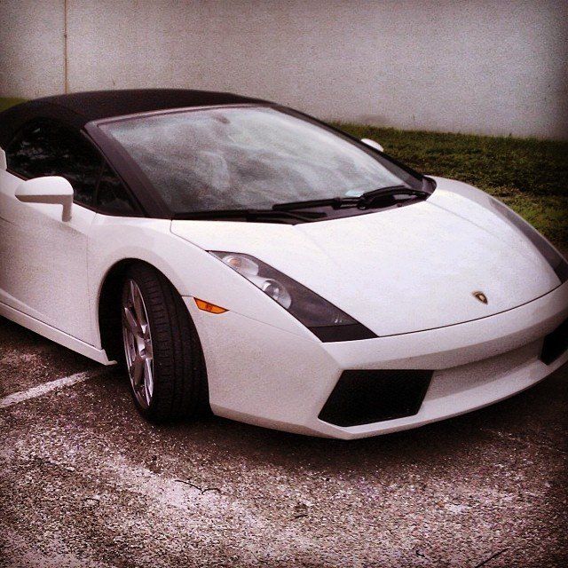 White Lamborghini convertible parked on pavement. Black top.