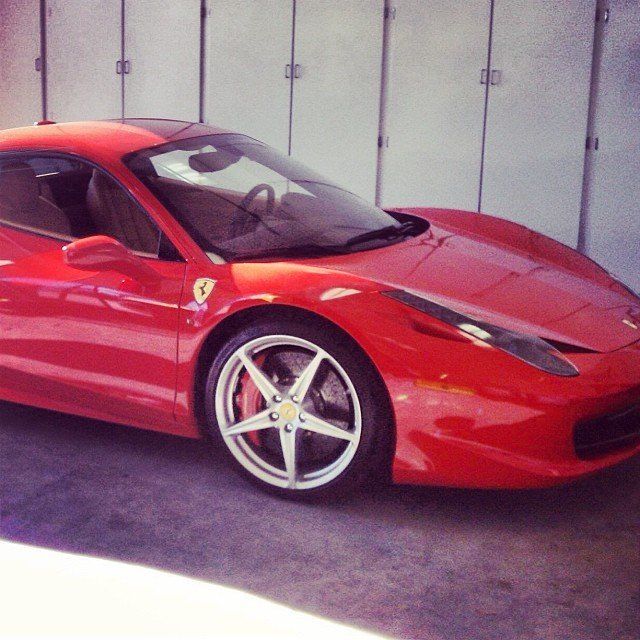 Red Ferrari sports car parked in front of closed white doors.