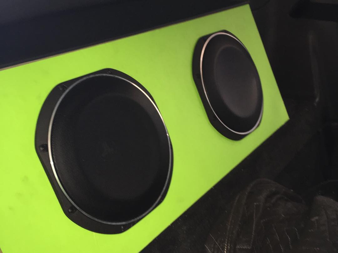 Two black speakers in a lime green box, likely for a car audio system.