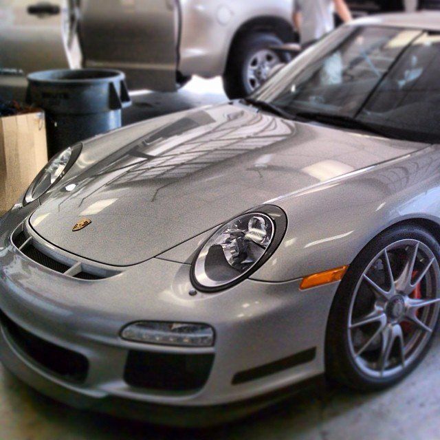 Silver Porsche sports car in a garage, parked near a truck.