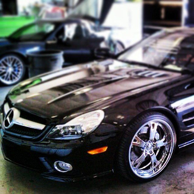 Black Mercedes SL convertible with chrome rims in a garage, other vehicles in background.