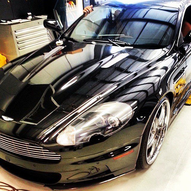 Black Aston Martin sports car with shiny chrome wheels, parked inside a garage.