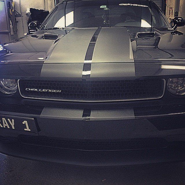 Black Dodge Challenger with gray racing stripes and custom license plate.