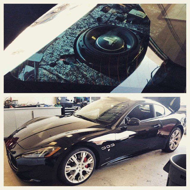 Black Maserati with aftermarket subwoofer installation in the trunk, in a garage setting.