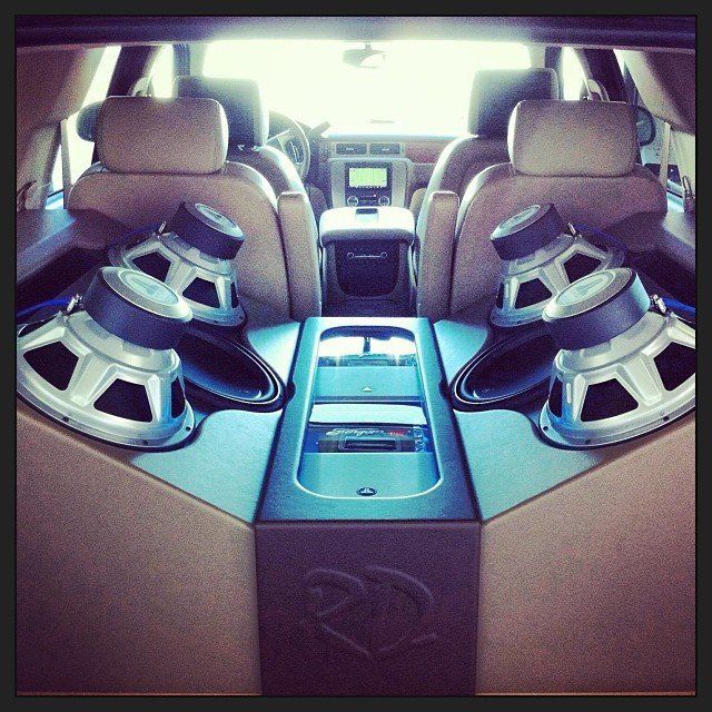 Back seat of a vehicle customized with two large woofers and a center console.