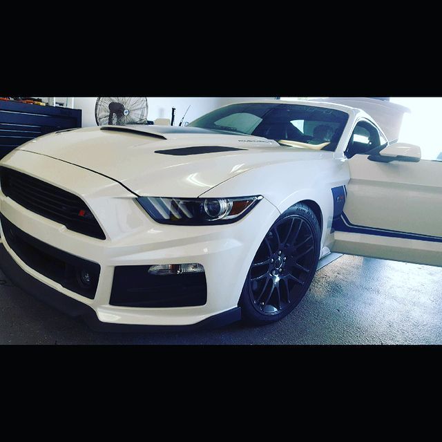 White Ford Mustang with black accents, door open, parked in a garage.