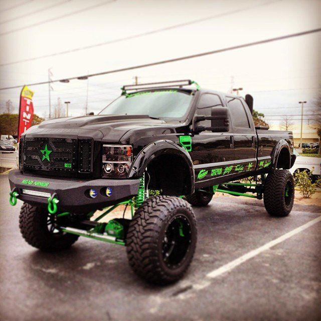 Black and green lifted truck parked in a lot, with large tires and custom grill and bumpers.