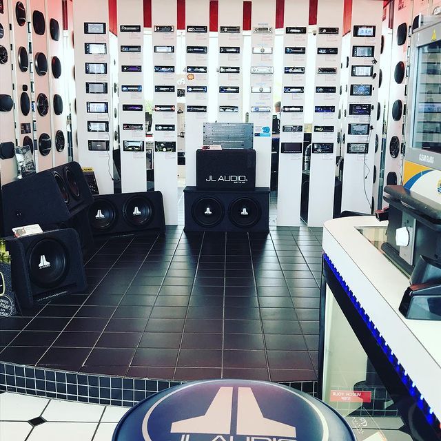 Interior car audio store display, featuring speakers, head units, and a JL Audio logo stool.