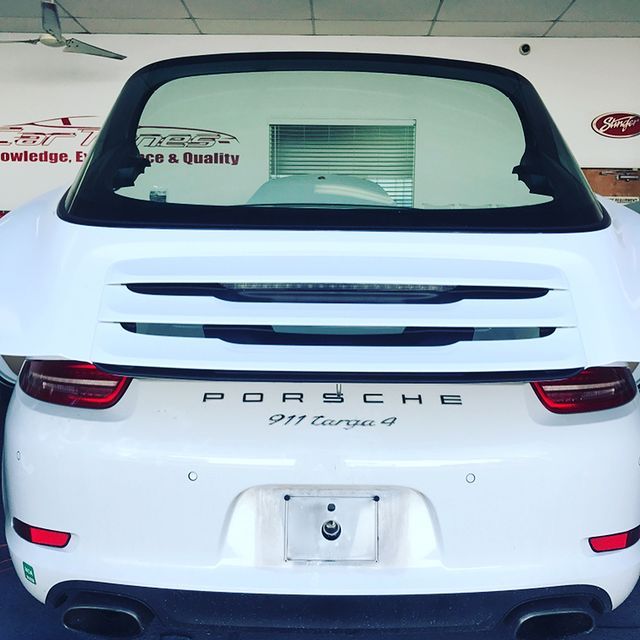 White Porsche 911 Targa 4 with rear window open, license plate, and dual exhaust in a shop.