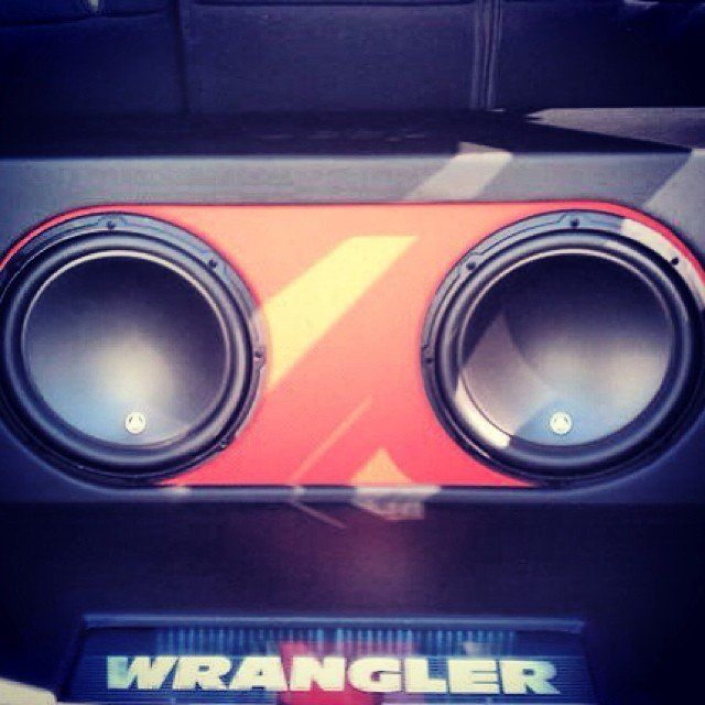 Two large black speakers mounted in a red and black panel in a Jeep Wrangler.