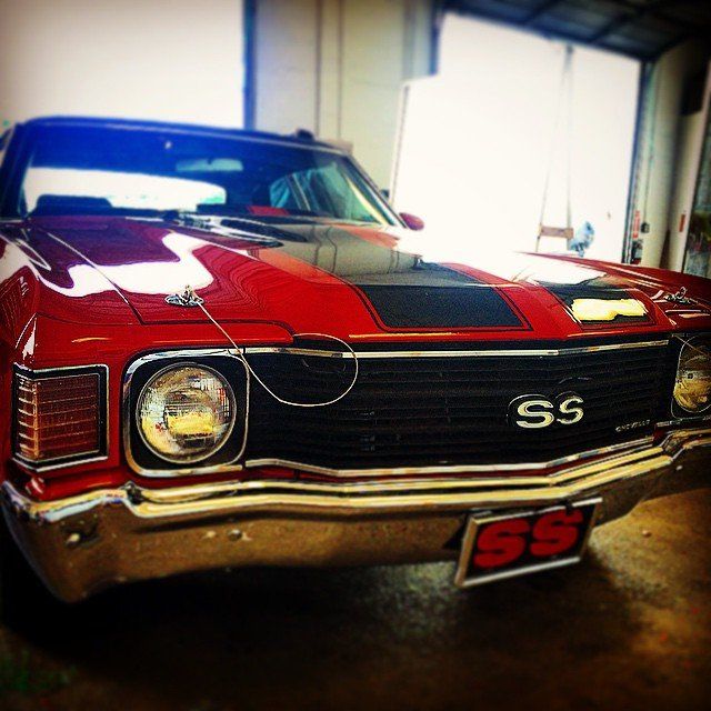Red Chevrolet Chevelle SS muscle car with black racing stripes, indoors.