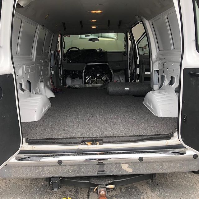 Interior view of an empty white cargo van with gray carpet flooring and open rear doors.