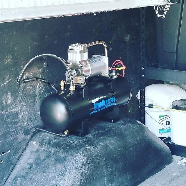 Black air compressor mounted inside a vehicle, with silver components and a black tank.