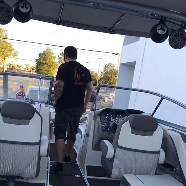 Man walking into a boat with gray and white seats, JL audio speakers, and steering wheel.