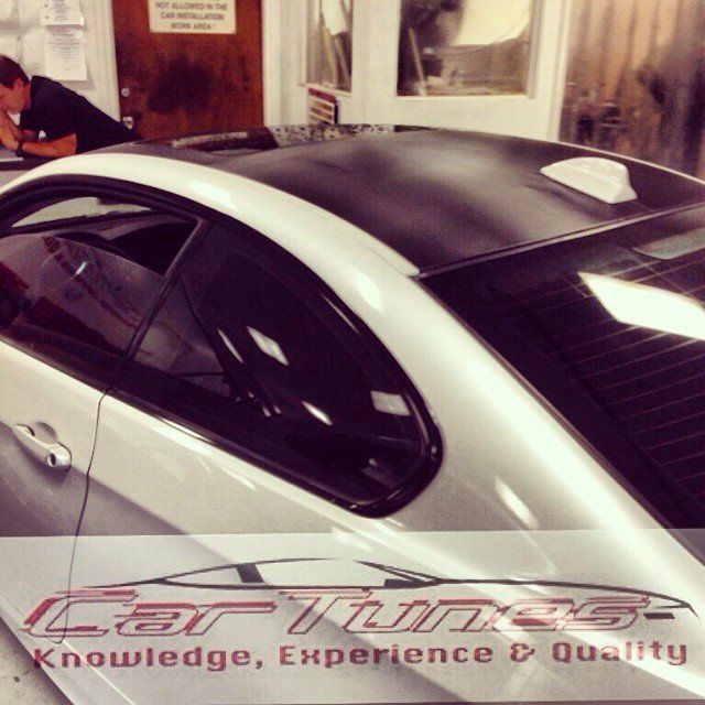 White car with black roof in shop, person working on it.