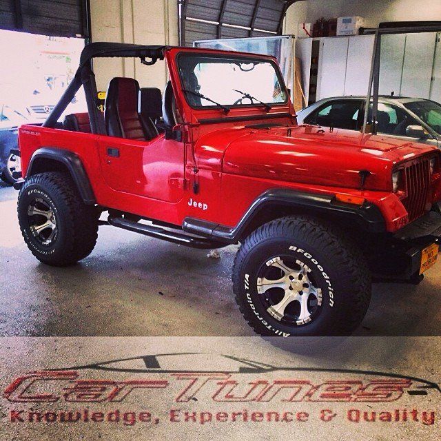 Red Jeep Wrangler inside a garage with roll cage, black accents, and off-road tires.