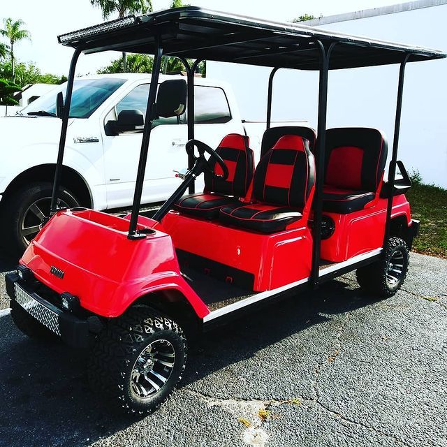 Red golf cart with black roof and seating, parked next to a white pickup truck.