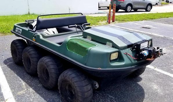 Green amphibious Argo vehicle parked on asphalt with black tires.