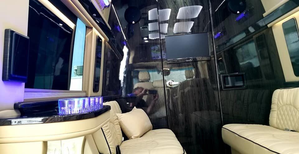 Luxurious van interior with cream-colored seating, dark wood paneling, and large screens.