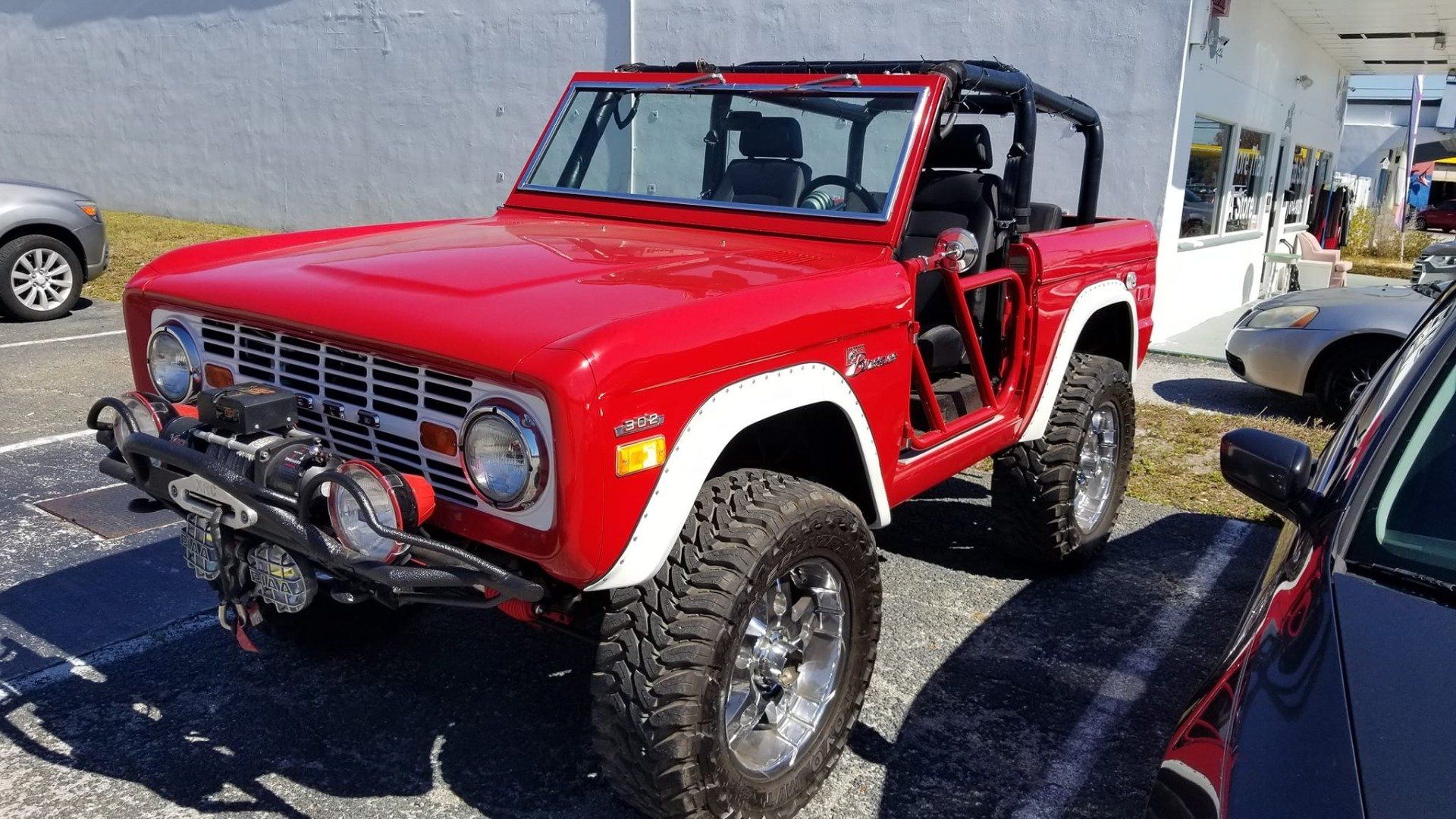 Red vintage Ford Bronco with white trim and large tires parked outdoors.