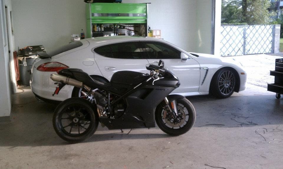 Black motorcycle parked in front of a white car inside a garage.