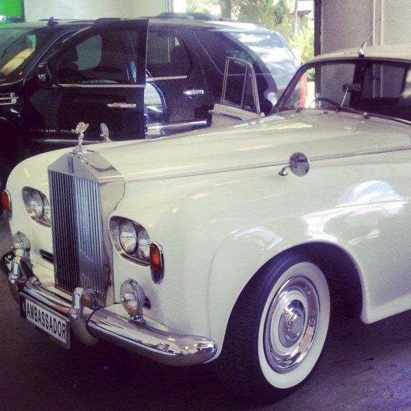 White Rolls-Royce with Ambassador license plate parked next to a black SUV.