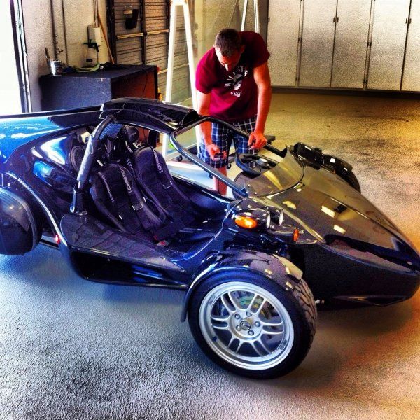 Man working on a blue three-wheeled vehicle in a garage.