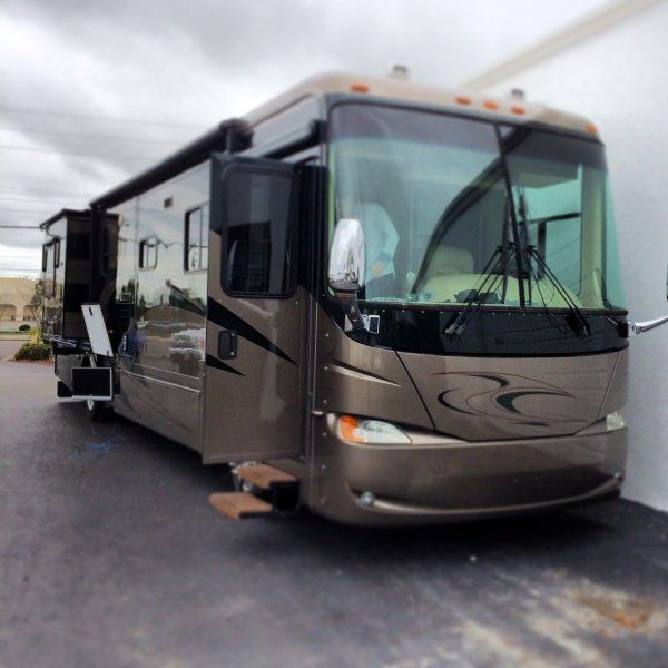 Brown RV parked on asphalt, slide-out extended, steps deployed.