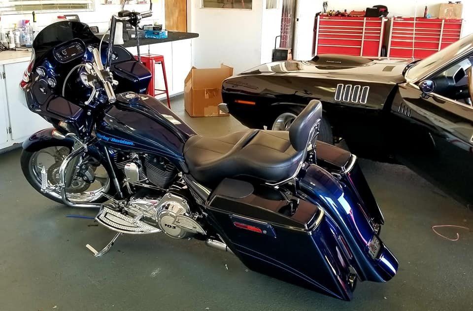 Blue Harley-Davidson motorcycle parked in a garage, near a black classic car and tool chests.
