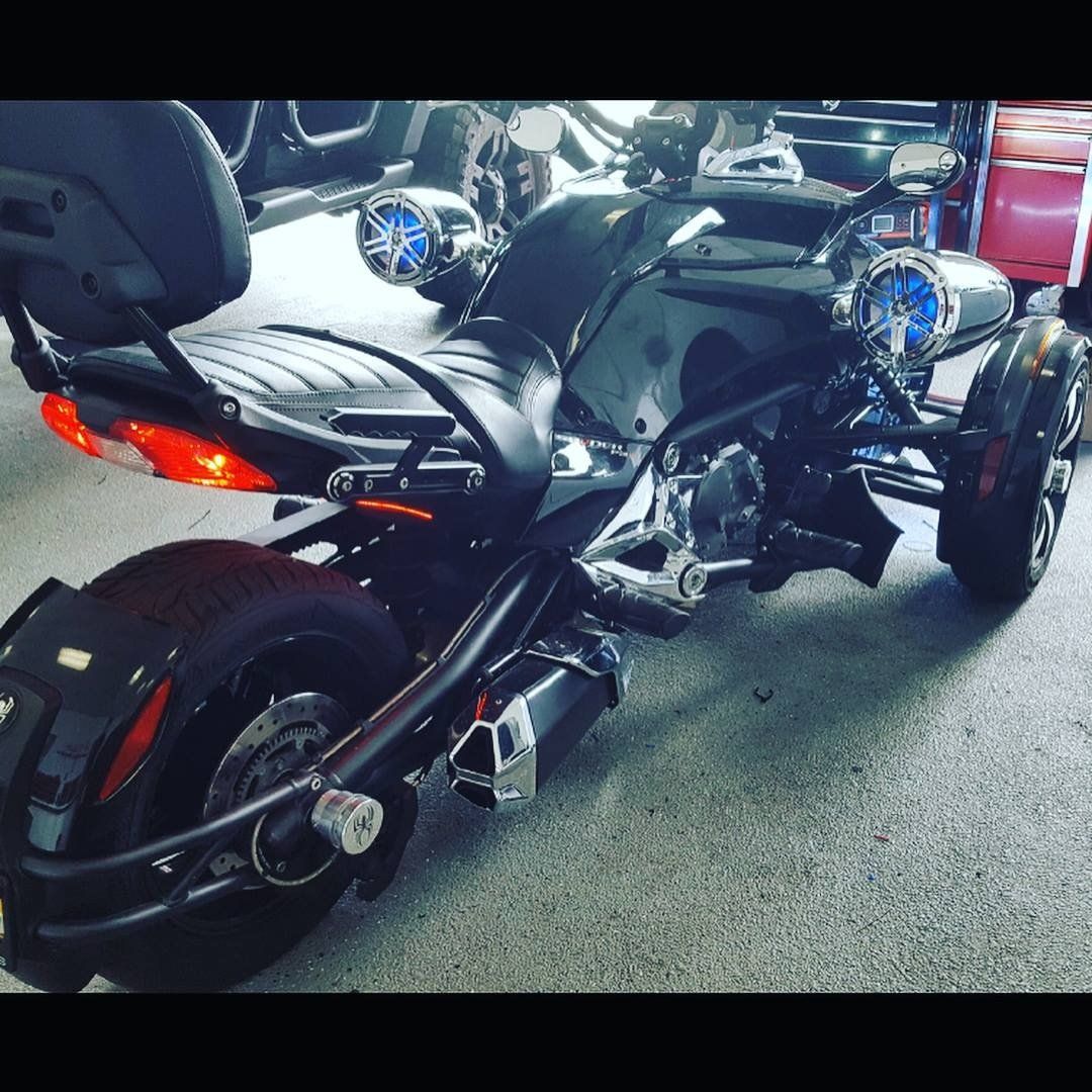Black Can-Am Spyder motorcycle with custom blue speaker lights parked indoors.